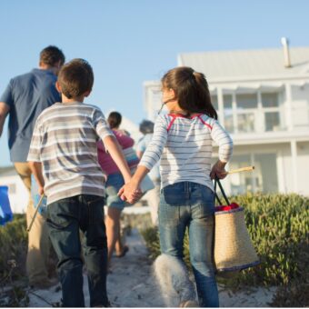 Children holding hands behind father walking up to a house.
